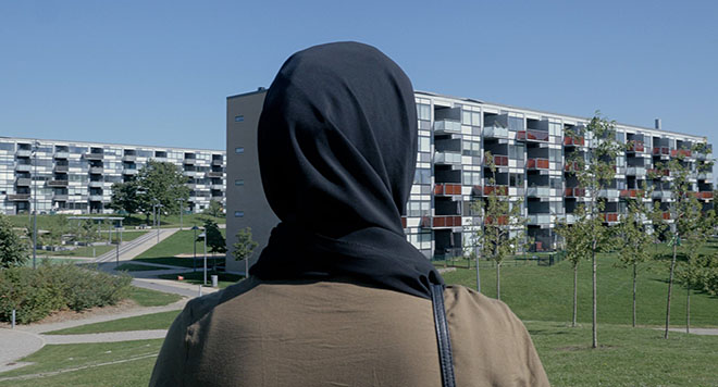 Kvinde med tørklæde skuer ud over et boligområde.