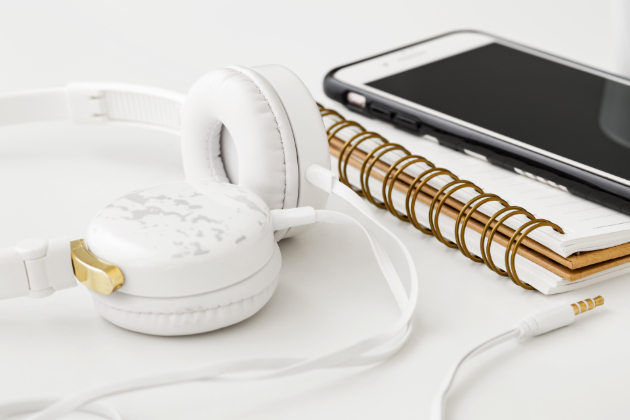 Dekorativt element: billede med en blok med spiralryg, et sæt hvide høretelefoner og en smartphone