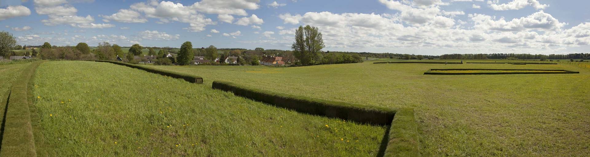 De store haller er markeret med græstørvsvolde, så man kan gå rundt i mellem dem og fornemme både de enkelte bygningers størrelse og størrelsen på hele gårdstoften. Foto: Ole Malling Se billedtekst.
