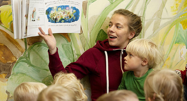 Voksen kvinde læser højt for en gruppe børn.