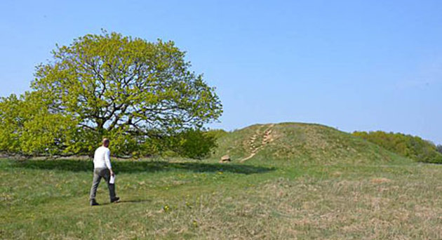 Foto af Egtvedpigens gravhøj, som det tager sig ud idag, græsklædt og med nærtstående egetræer og hasselkrat