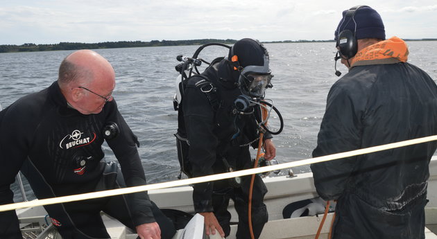 Foto af 2 arkæologer på båd, den ene iført dykkerudstyr og klar til at kommer i vandet ved Århus Bugten.