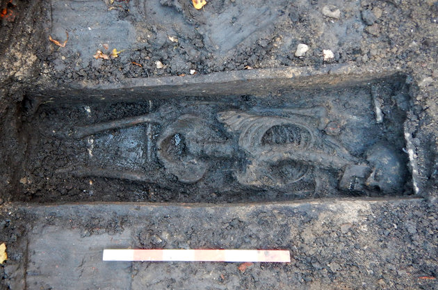Foto af bevaret kistegrav, hvor det mørknede skelet ligger på ryggen med hovedet let drejet til den ene side