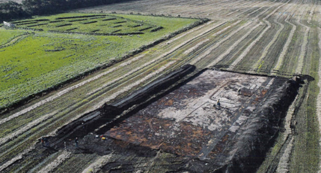 Luftfoto af Udgravning af gården med de to hustomter og den mindre hustomt. I baggrunden ligger den rekonstruerede Lyngsmose-fæstning. Foto: Esben Schlosser Mauritsen 