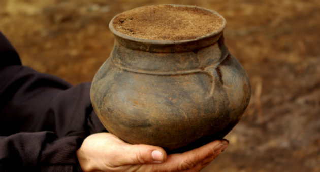 Nærbillede af en arkæologs hænder, der holder en netop udgravet intakt urne