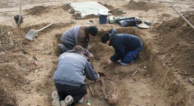 Foto af tre arkæologer, der omhyggeligt udgraver en mandsgrav.