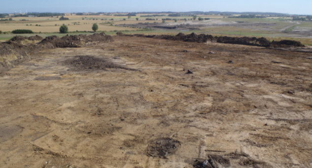 Billede af mark, hvor muldlaget er gravet af. I det blotlagte sand ses mørke spor efter fra tidligere tider.