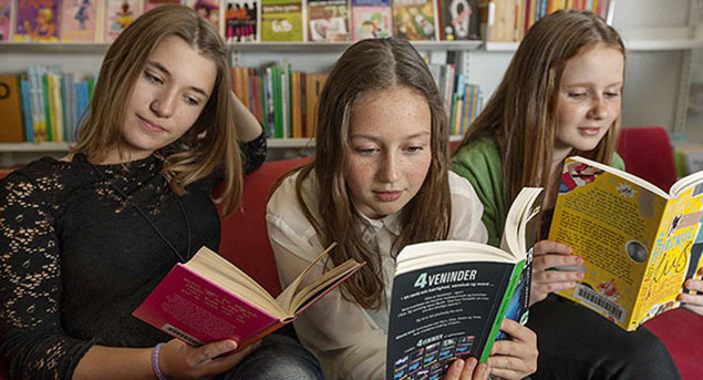 Tre piger læser på biblioteket