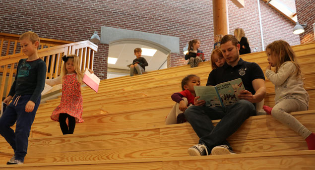 Børn og voksne sidder på en meget stor trappe og læser.