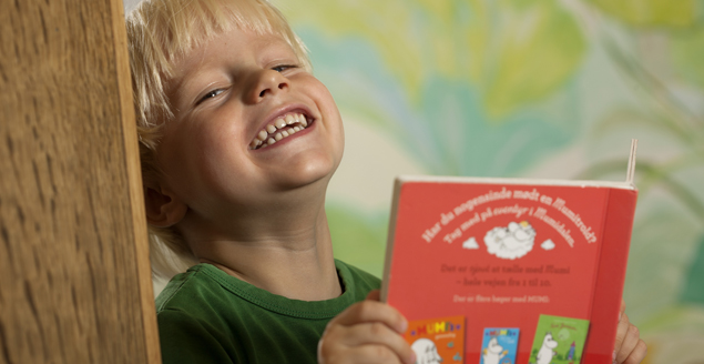 Barn læser i bog og griner. Foto: Ballerup Bibliotek, Mikal Schlosser
