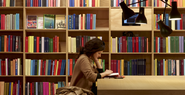 Foto af kvinde, der læser en bog på bibliotek.