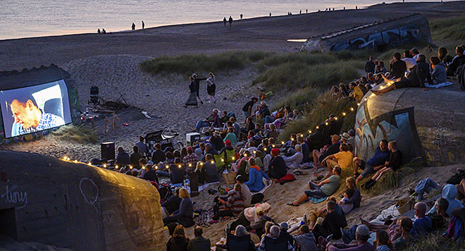Mennesker på stranden ser film projiceret op på en bunker.